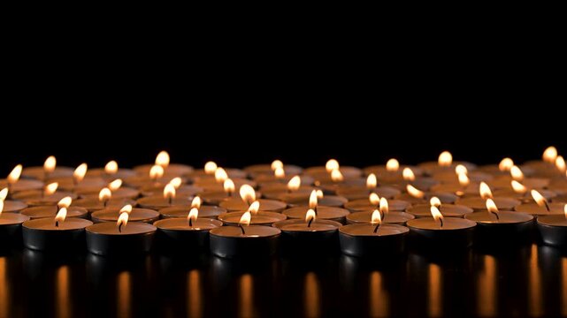 View of many small candles burning against dark background