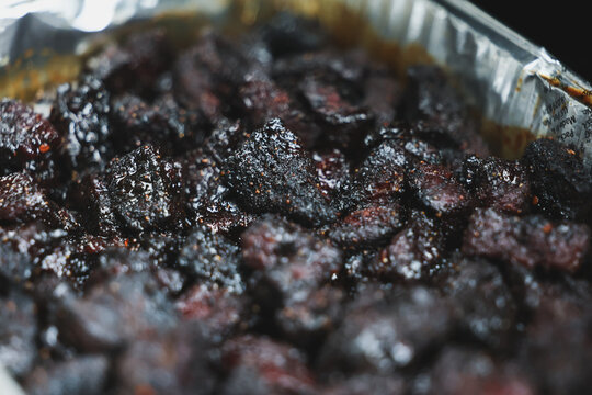 Pork Belly Burnt Ends cooked until black on a pellet grill smoker. The delicious morsels of fatty pig meat are resting in a tinfoil pan ready to eat for dinner. 