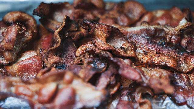 Crispy bacon covered in grease and hot oil for breakfast. The delicious pork belly is tasty food and ready for a meal. 