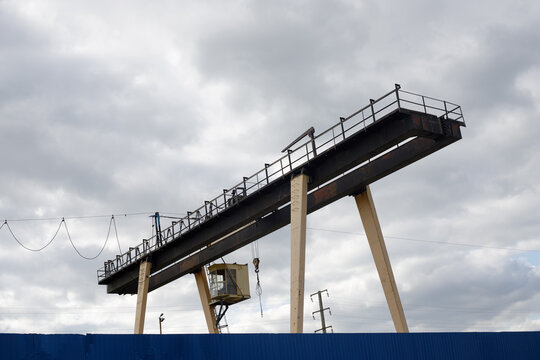 Large, powerful industrial overhead crane for loading rail cars. The steel beams supporting the beige outriggers, operator's cabin