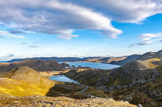 Scenic panoramic view of the arctic landscape near North Cape, Norway. Rugged mountains, blue fjords, and tundra under a dramatic sky with soft sunlight