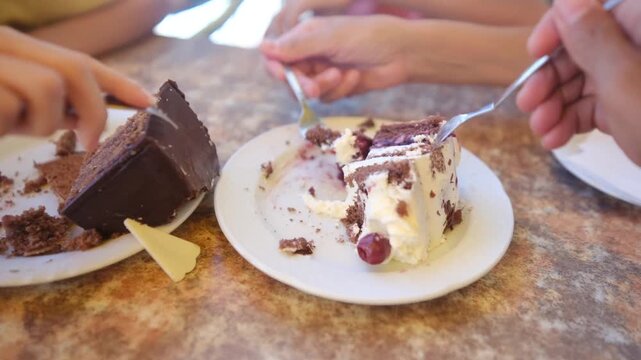 People eating black forest and sachertorte cake slices in a cafe. A person's hand with a fork breaking off a piece of dessert with cherries and whipped cream for a sweet snack