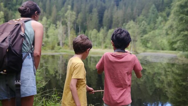 Adventurous mother and sons hiking together in a national park, stopping to admire a beautiful mountain lake and take pictures of the scenic landscape reflecting in the water