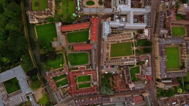 4K top-down aerial view of Cambridge University college quadrangles with manicured lawns, historic courts and punts on the River Cam in England.