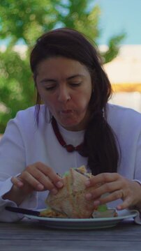 Woman eating gourmet burger with french fries at outdoor restaurant table during sunny summer afternoon conveying casual dining leisure