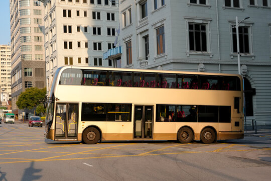 A beige double-decker bus turns at a city street intersection on its route
