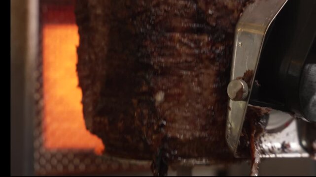 Close-up of a professional cook shaving thin slices of meat off a rotating doner kebab grill, fa01