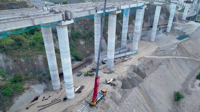 Drone tracking heavy machinery and labor on concrete overpass site. Dynamic aerial drone footage capturing active heavy civil engineering