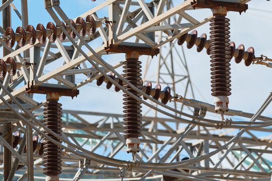 Close-up of ceramic insulators and steel support structures inside electrical substation. Industrial infrastructure used for electrical isolation and high voltage transmission systems.