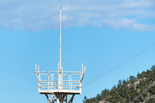 Lightning protection mast installed on a steel structure at an electrical substation under blue sky. Utility infrastructure used to protect high voltage equipment from lightning strikes.