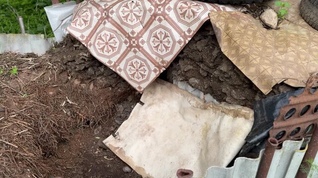 The compost manure pile has a fence made of slate sheets and is covered with pieces of linoleum on the street in the summer cottage