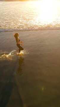 Aerial shot of a fit asian woman jogging on the beach at sunset in Southern California. Vertical Video.