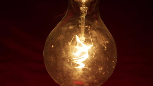 Glowing light bulb illuminates the darkness with a warm macro view of its burning tungsten filament. Concept of bright ideas, creative inspiration, authentic innovation, and electrical energy.