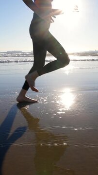 Athletic Asian woman jogging on the beach at sunset in Southern California. Slow motion. Vertical Video.