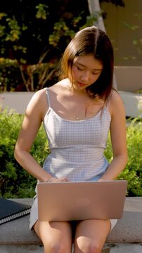 Asian female college student working on her homework while sitting on a bench outdoors