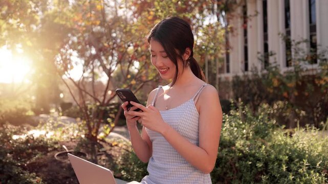 Pretty Asian college student take a break from studying to check her social media on her phone.