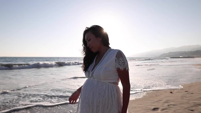 Attractive pregnant Asian woman enjoys a walk on the beach.