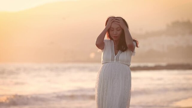 Attractive pregnant Asian woman enjoys a walk on the beach.