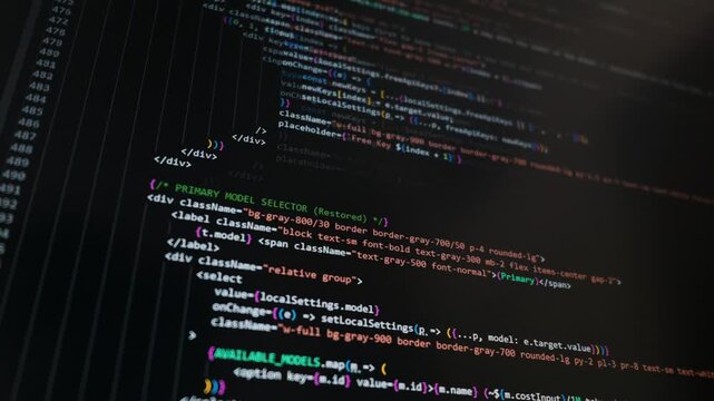 Colorful programming text scrolls automatically across a dark computer monitor interface. The complex script features machine learning API configurations and web development frameworks.
