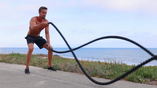 Athletic man working out with a battle rope at the beach in Southern California. Slow Motion.