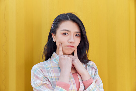 Playful young woman pouting against yellow wall