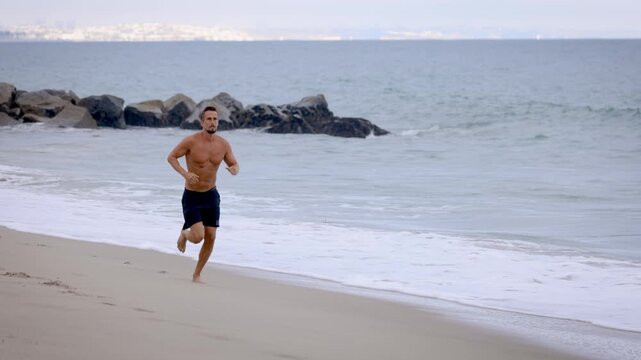 Athletic man jogging at the beach in Southern California. Slow Motion.