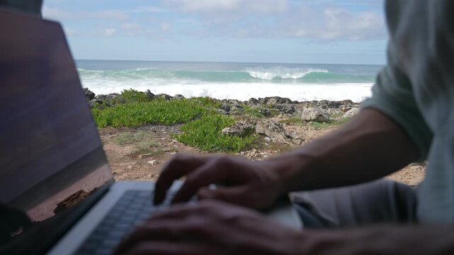 Working on Laptop near to the Ocean, hands of Men working on computer at Coast with Sea Surf, digital nomad remote work.