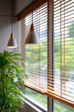 modern windows with blinds and pendant lights in the office, wooden slats on window frames, sunlight shining through, green plants outside the glass