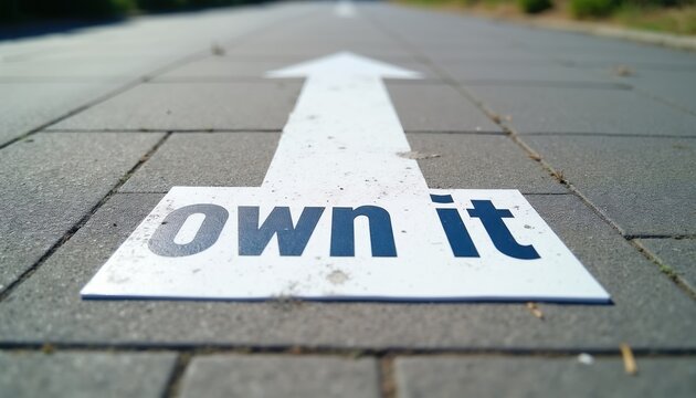 White arrow sign points forward on paved path with text own it. Symbolizes motivation, direction, and taking responsibility for ones journey.