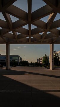 Vertical video: Framing canopy with two columns casting long shadows on campus, low sun lens flare