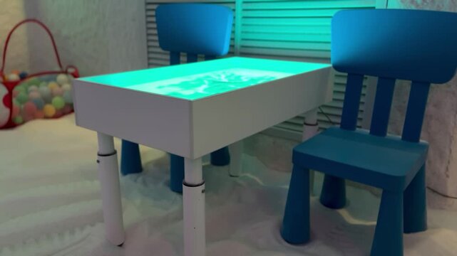 Salt floor children chair and table glowing halotherapy panel, soft blue ambient light, basket of colorful balls, white granular