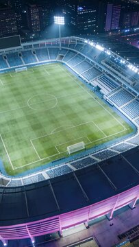Vertical video: Revealing drone moving over stadium at night, showing lit pitch and floodlights
