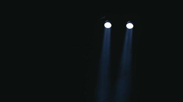 Minimalist shot of two parallel cold light beams cutting vertically through pitch black darkness. Smooth downward camera motion tracks past the fixtures to reveal subtle stage smoke