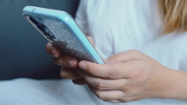 Close up of a person's hands holding a modern blue smartphone with a decorative glitter case, actively engaging with the device for communication, digital services, or browsing various applications