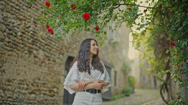 Young Woman Smiling Under Blooming Red Roses in Historic Alley