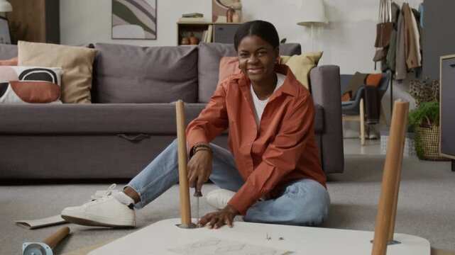 Portrait of cheerful African American girl smiling for camera while assembling wooden coffee table in living room