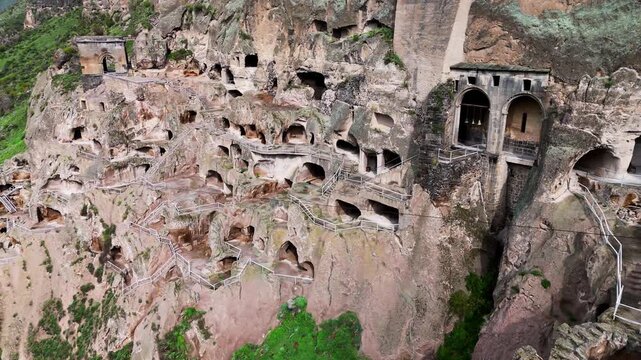 Drone flight past Vardzia cave monastery sanctuary in Georgia. Aerial view of the stone bell tower and ancient rock-hewn church complex carved into the steep Erusheti Mountain cliffside