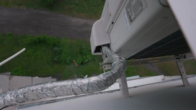 An insulated pipe connects to an outdoor air conditioner compressor mounted high on a building wall. Concept of residential climate control, HVAC installation, and summer cooling.