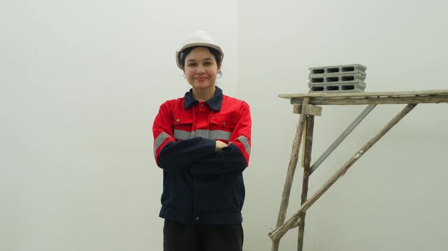 Female worker hard hat standing with crossed arms near scaffold and concrete block construction site, safety helmet, industrial workspace, renovation labor, concrete block, scaffold, adult