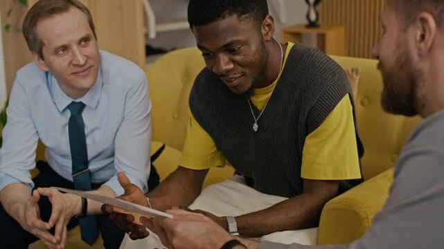 Caucasian man chatting with best friends, telling about son and showing his drawing to them while they spending time in living room