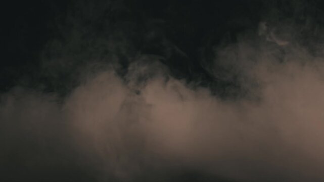 Static low angle shot of dense theatrical smoke and fog billowing heavily across a dark stage floor. Soft semi-warm white lighting creates a textured