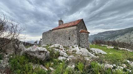 Fototapeta premium Stone chapel on charred hillside near Sutomore Montenegro with regrowing wildflowers