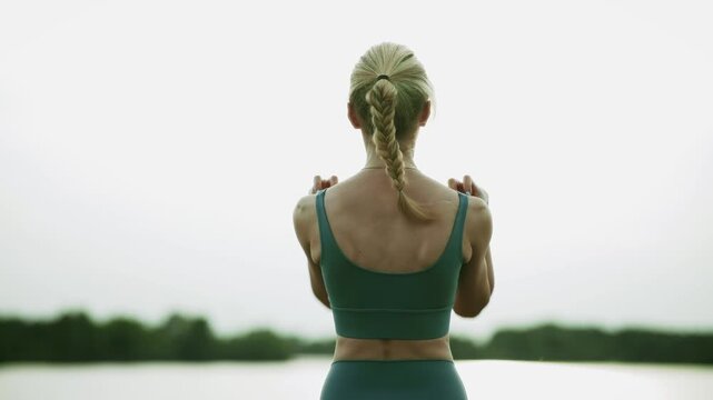 Sportswoman Warming Up Shoulders and Doing Joints Exercises Near Lake. Stretching Back Muscles