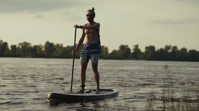 Surfer Standing on Inflatable Board and Paddling on River. Surfing Athlete Balancing on Water Surface with Paddle