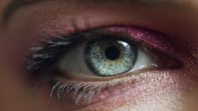 Close-up view of a woman's eye with colorful makeup as she opens and closes her eyelid during a makeup session at a home setting