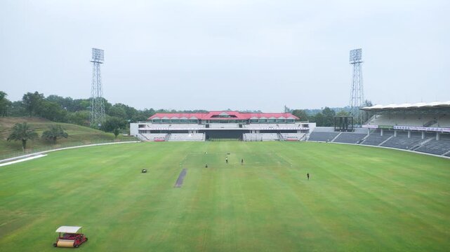 High angle establishing shot of a massive empty cricket stadium with floodlight towers and green field