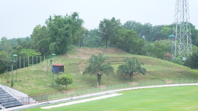 Natural green hill gallery with lush trees and steel tower at sports facility
