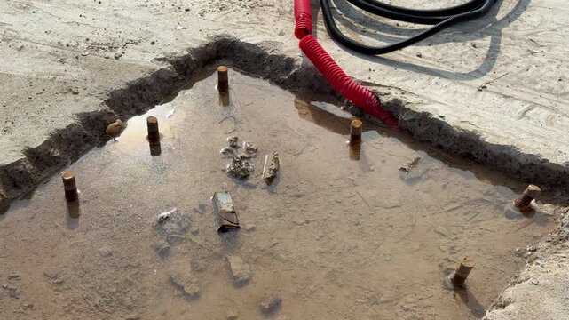 Ground hole with bolts and cable installer preparing concrete foundation for vertical billboard pole, coiled power cable