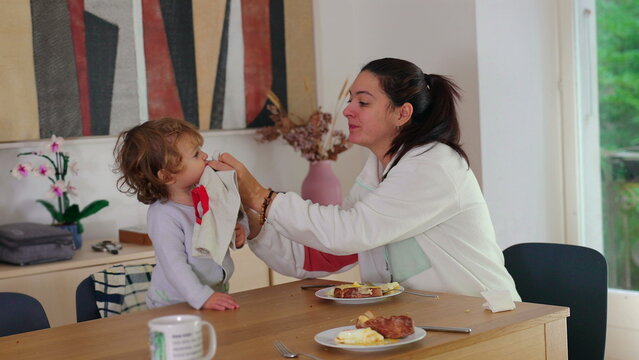Mother gently wiping toddler face with napkin after meal at dining table sharing caring parenting moment and nurturing family connection at home