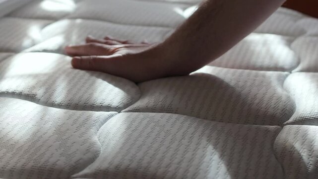 A man presses hard with his hand on a new orthopedic mattress, assessing its quality before purchasing it in a store, slow motion video